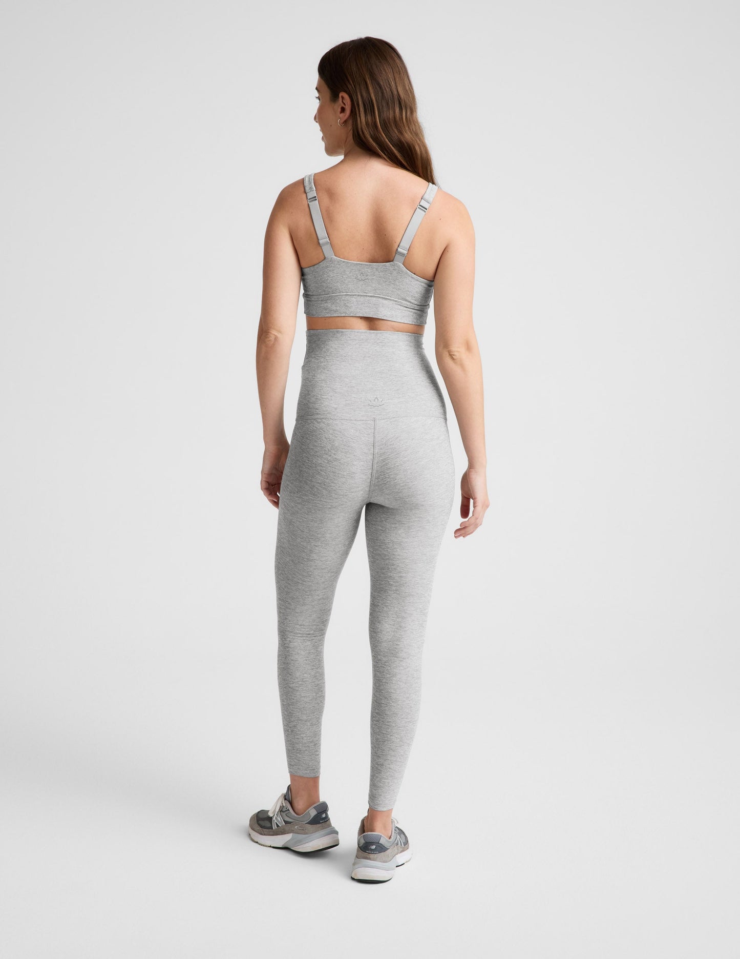 Pregnant woman wearing a gray bra and leggings on a plain background.