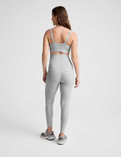 Pregnant woman wearing a gray bra and leggings on a plain background.