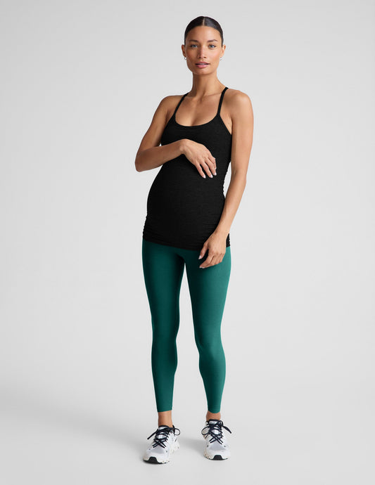 Woman wearing a black tank top and green maternity leggings on a light gray background.