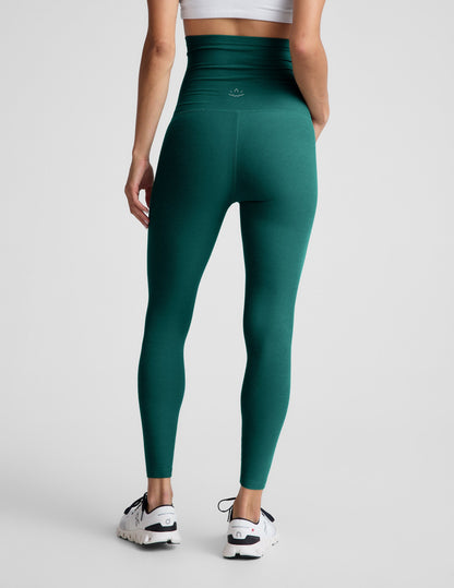 Woman wearing green maternity leggings on a light gray background.