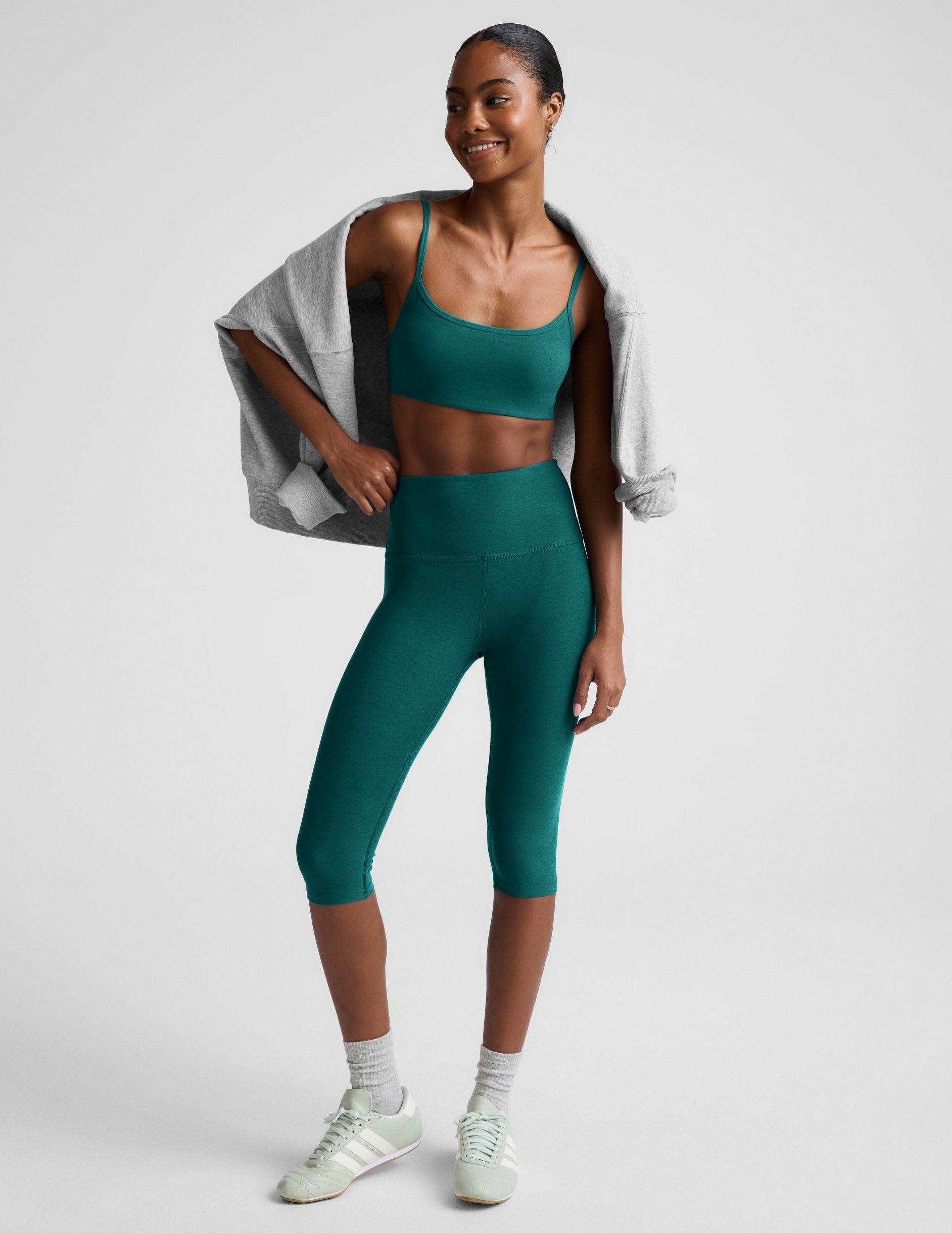 Teal Spacedye Pedal Pusher High Waisted Legging worn by a smiling model with a matching bra and draped grey sweatshirt.