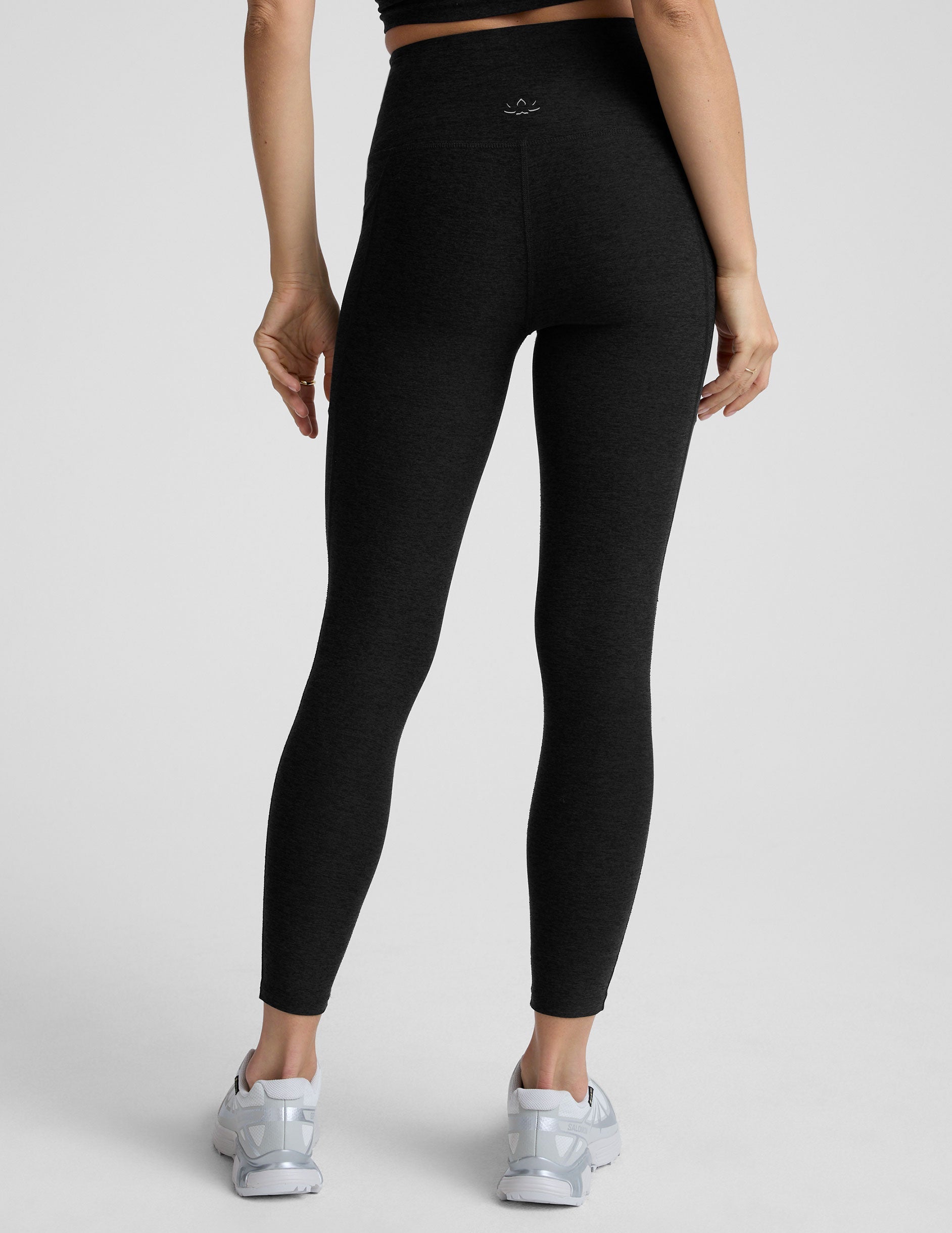 Woman wearing black pocket midi length leggings on a light gray background.
