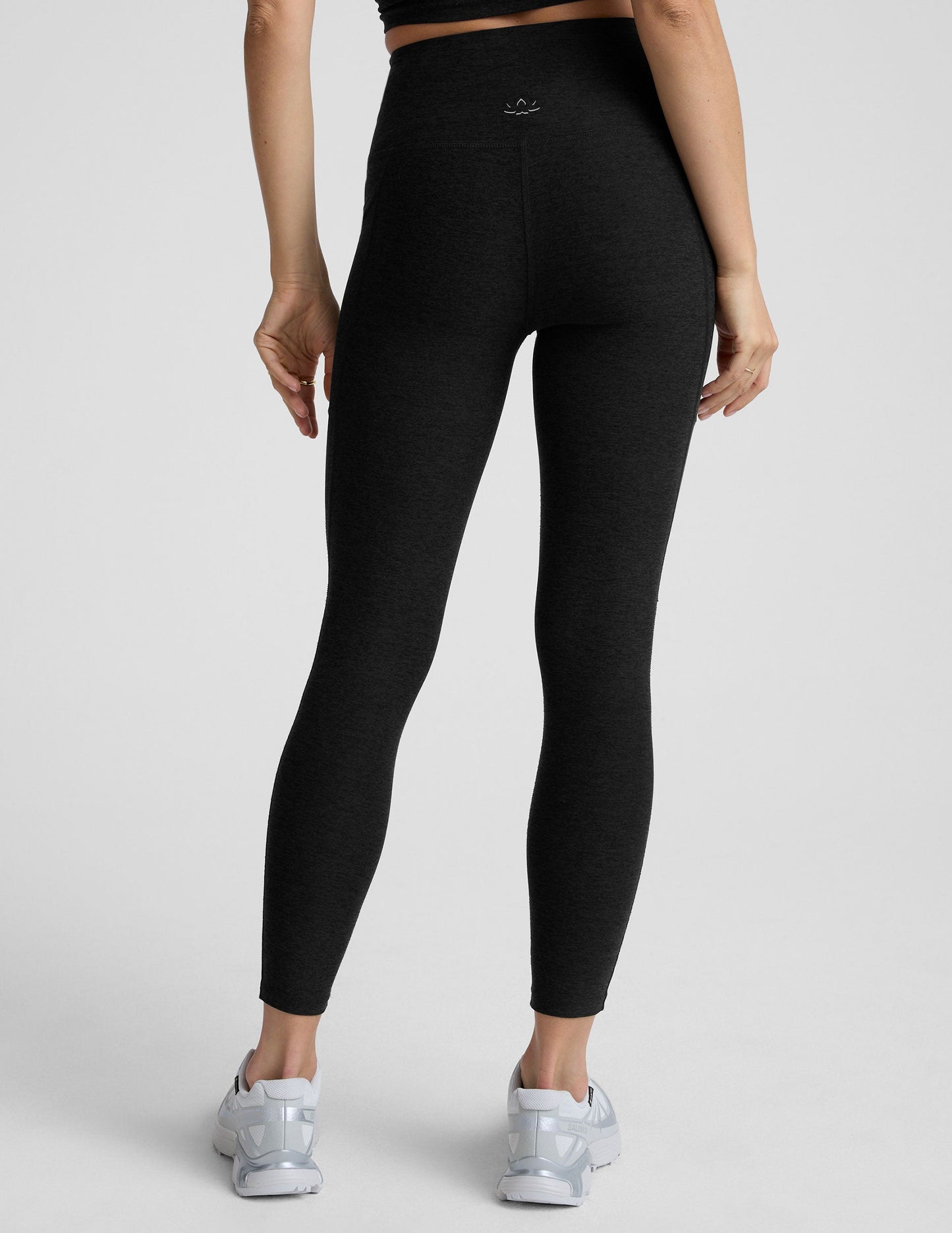 Woman wearing black pocket midi length leggings on a light gray background.