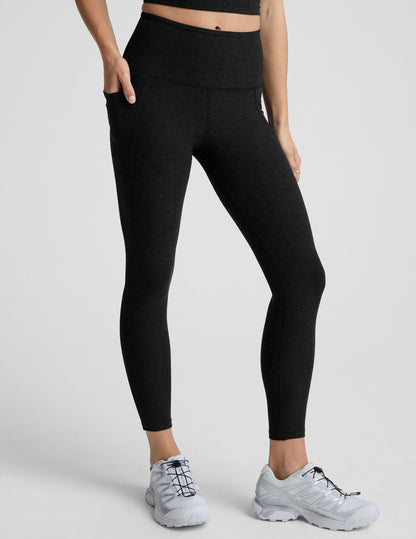 Woman wearing black pocket midi length leggings on a light gray background.