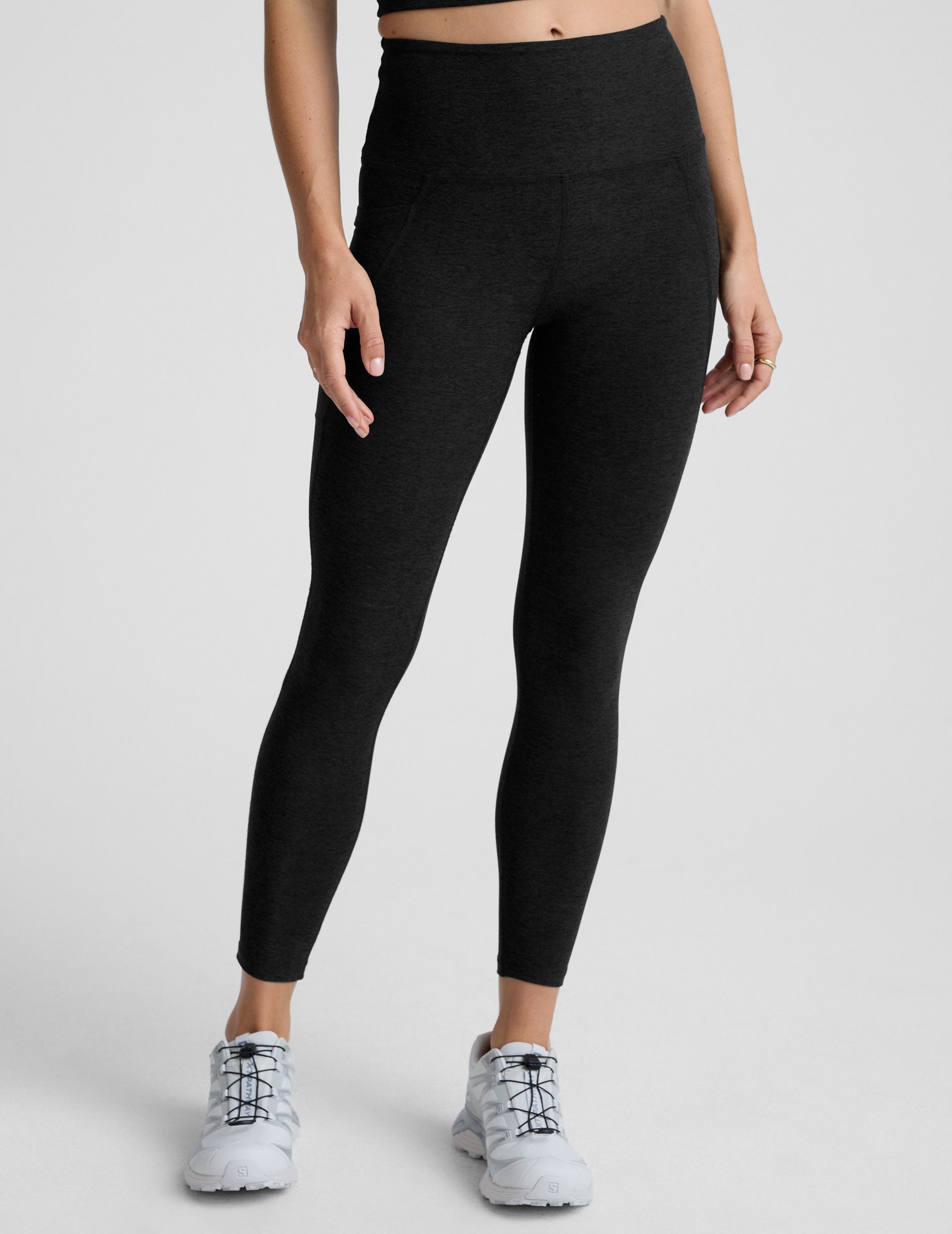 Woman wearing black pocket midi length leggings on a light gray background.