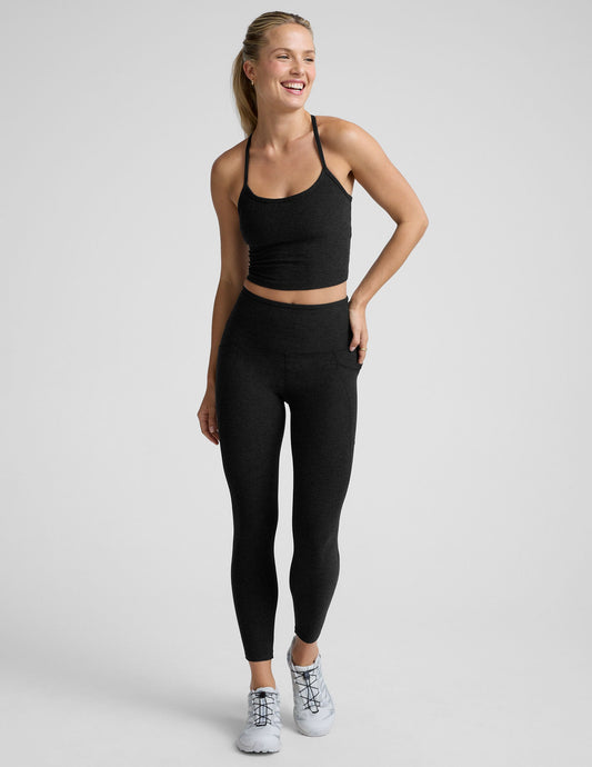 Woman wearing a black cropped tank and black pocket midi length leggings on a light gray background.