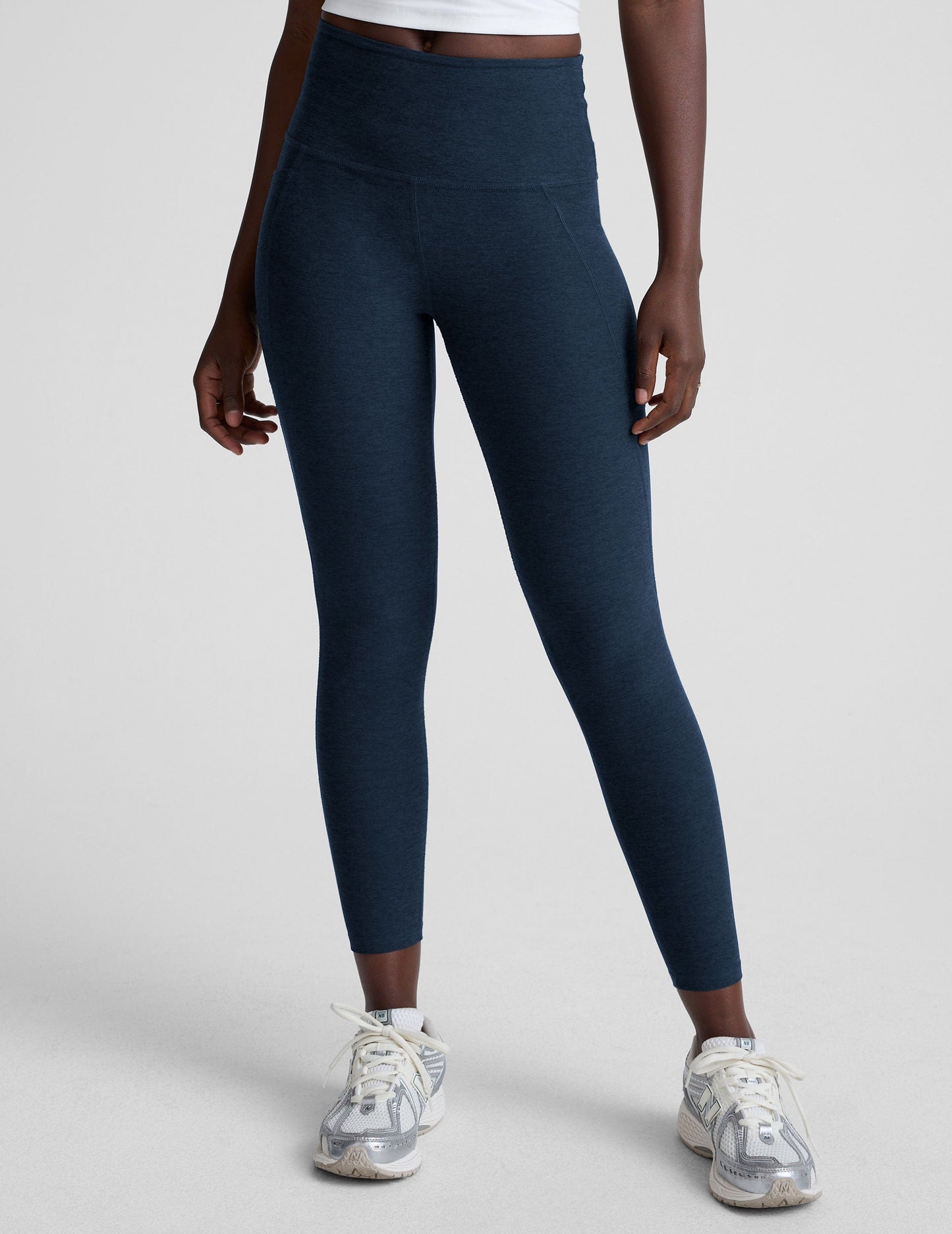 model is wearing blue high-waisted midi length leggings with side pockets on a light gray background.