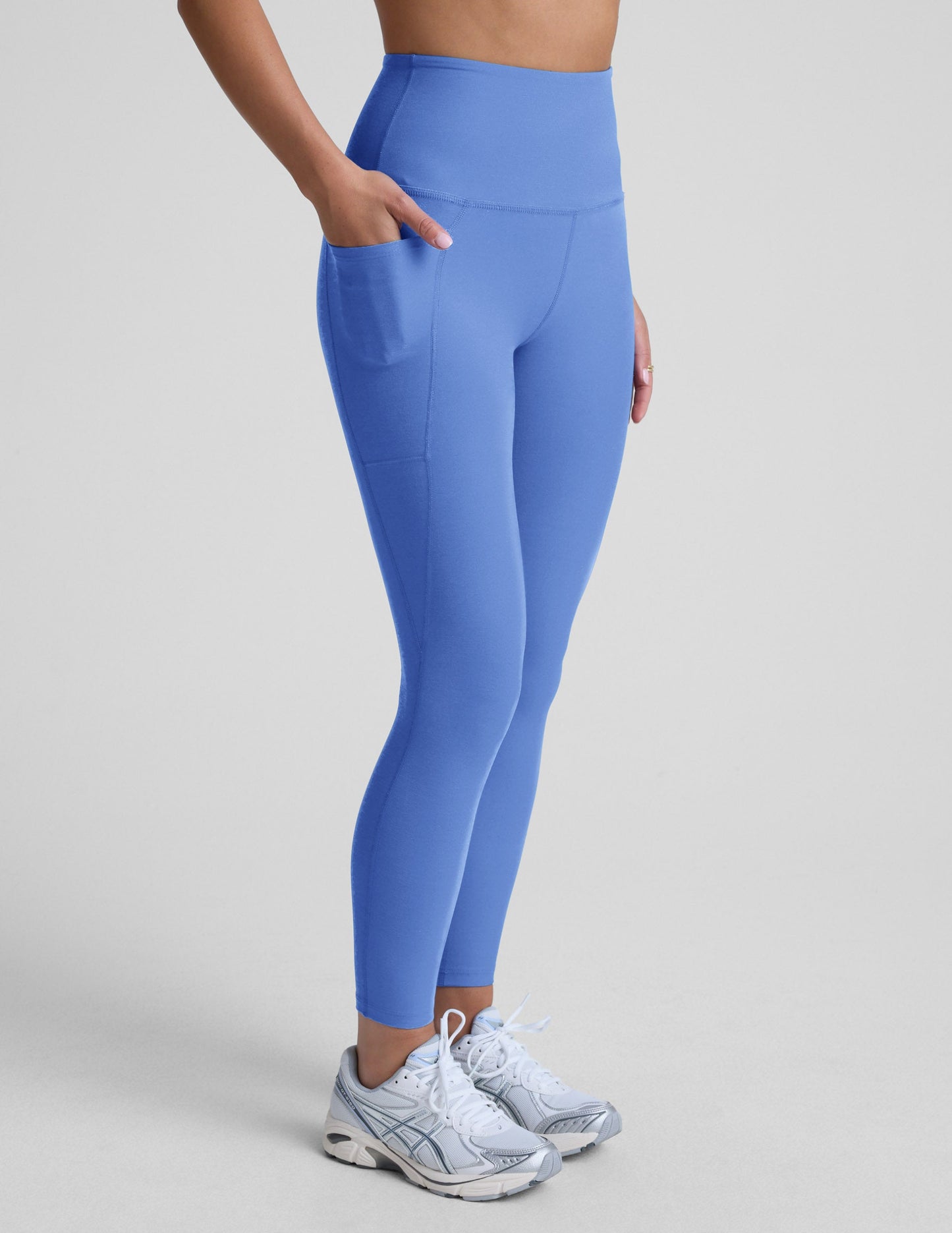 Woman wearing blue midi leggings with pockets against a light gray background.