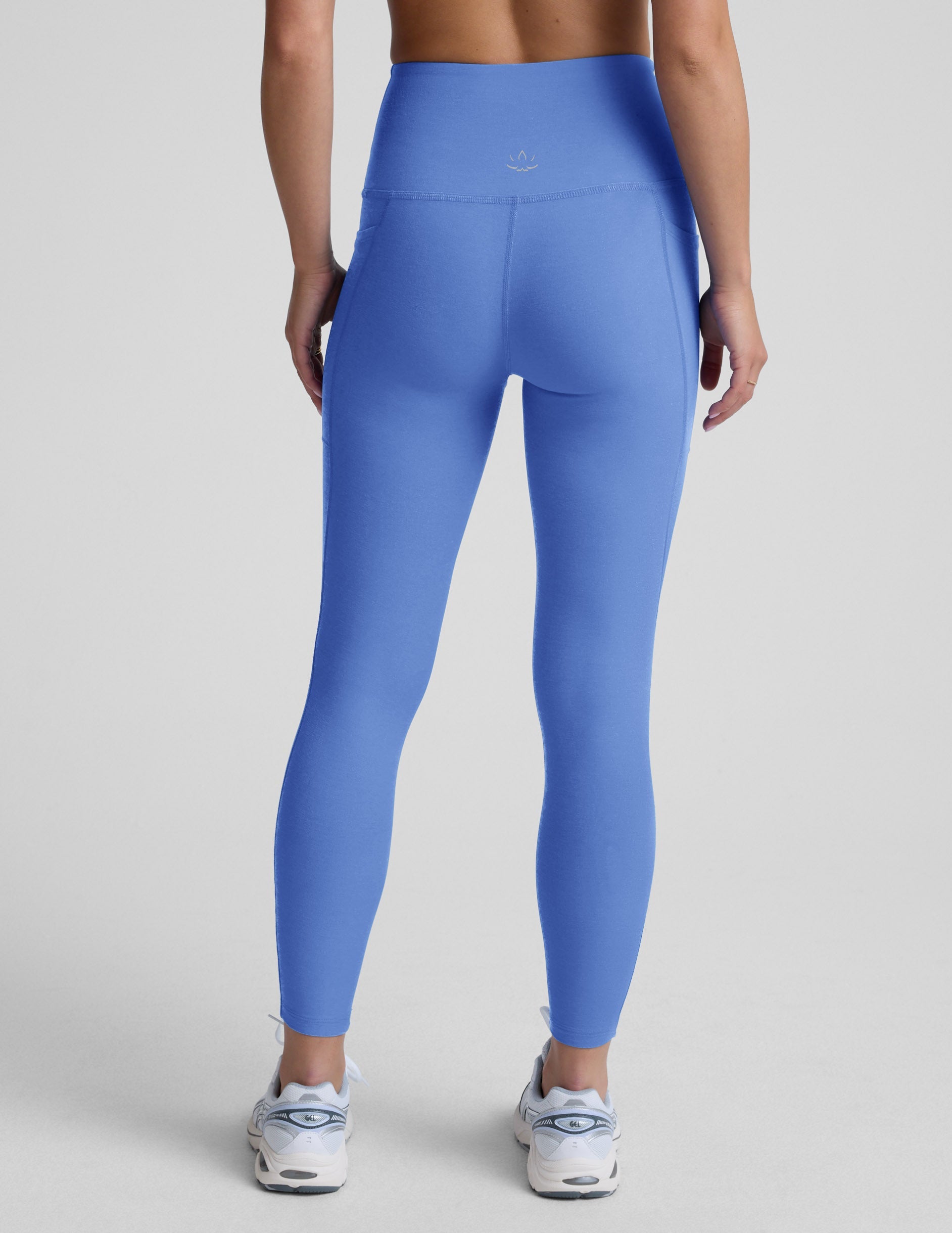 Woman wearing blue midi leggings with pockets against a light gray background.
