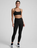 Woman wearing a black sports bra and leggings on a light gray background