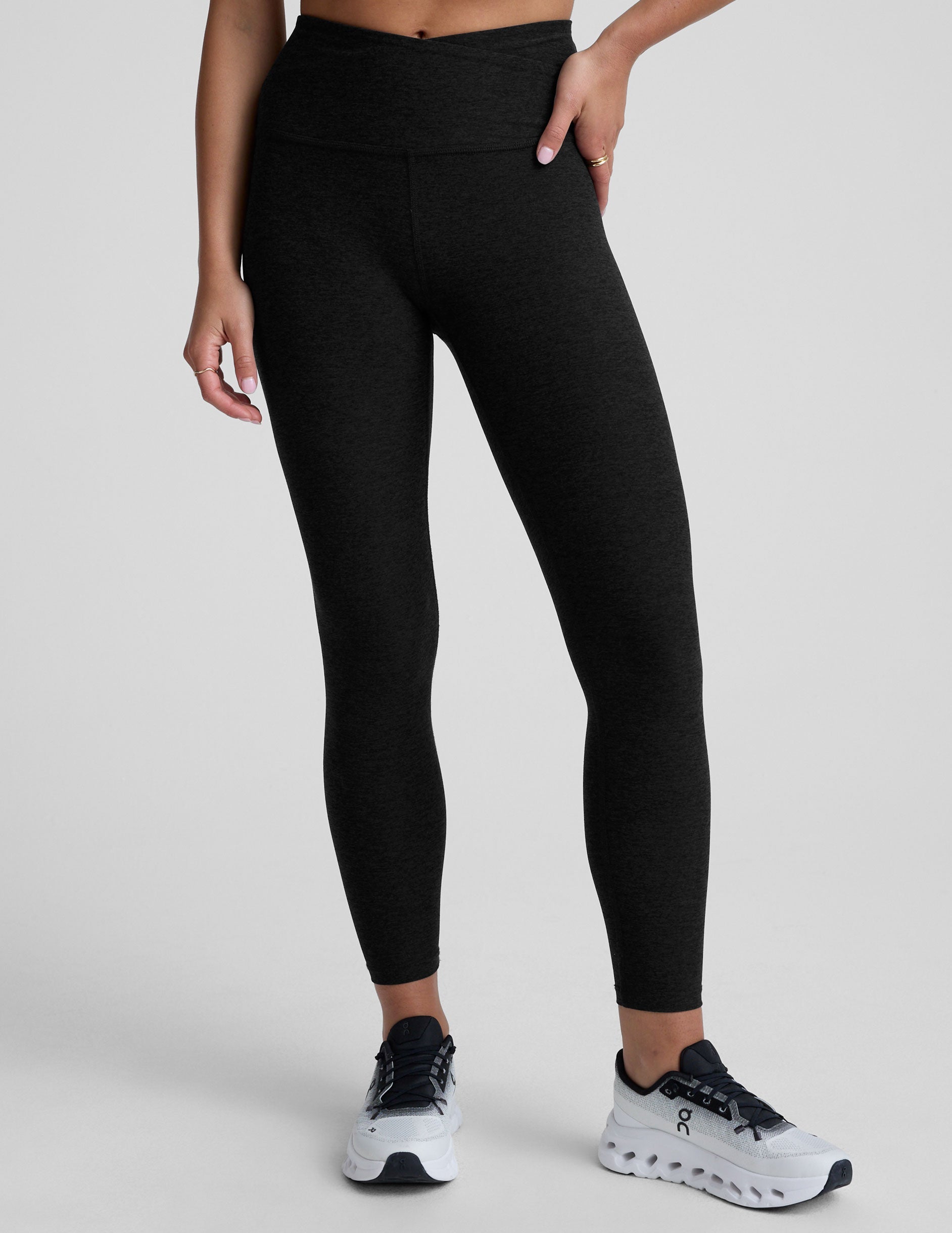 Black leggings with a front crossover waistband worn by a person on a light gray background.