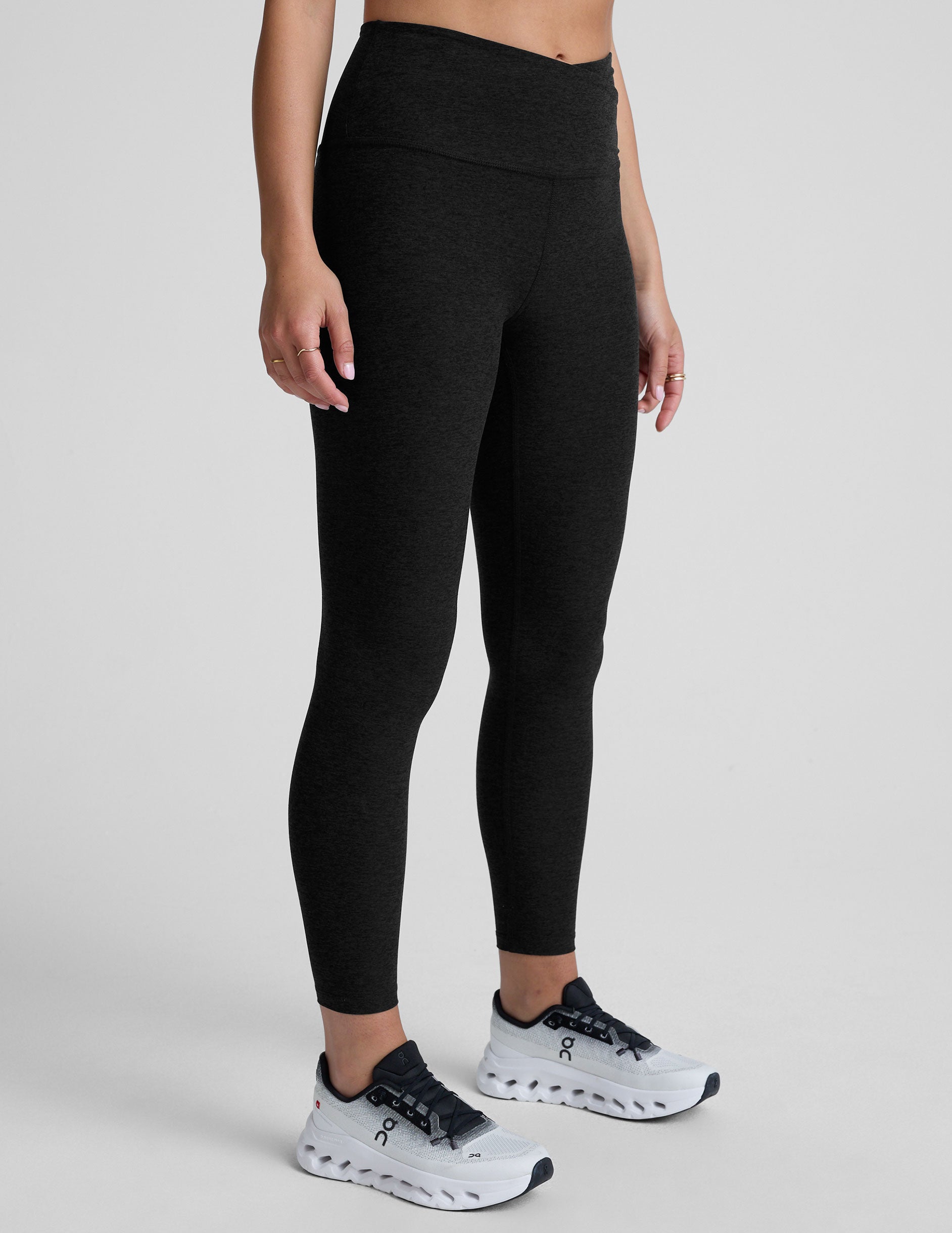 Black leggings with a front crossover waistband worn by a person on a light gray background.