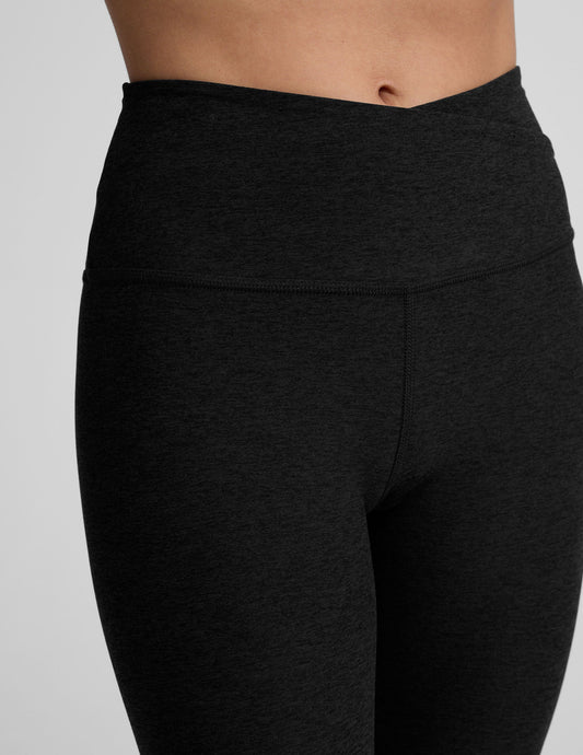 Black leggings with a front crossover waistband worn by a person on a light gray background.