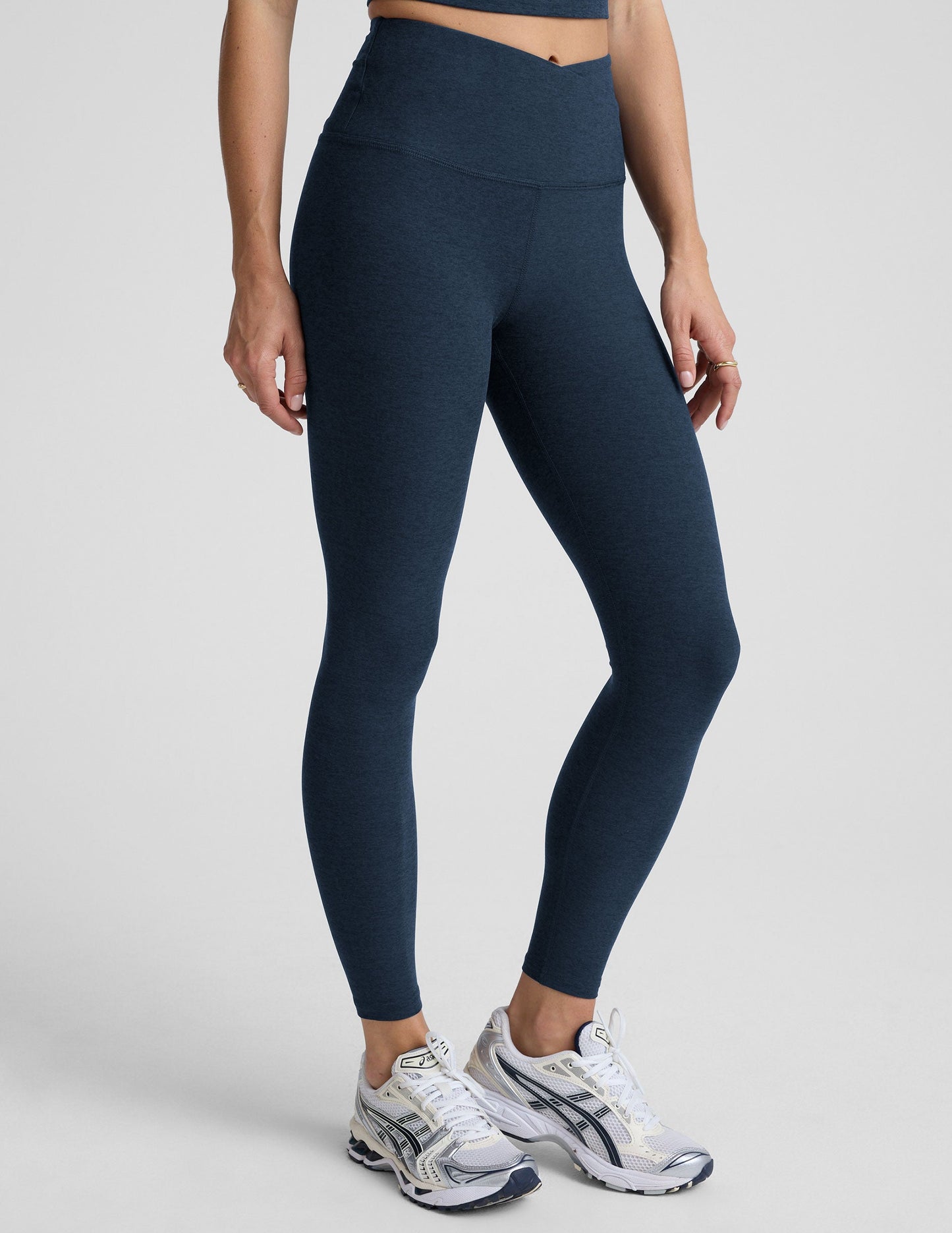 Person wearing navy blue leggings with a front crossover waistband on a plain background.