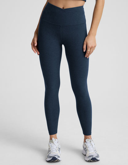 Person wearing navy blue leggings with a front crossover waistband on a plain background.