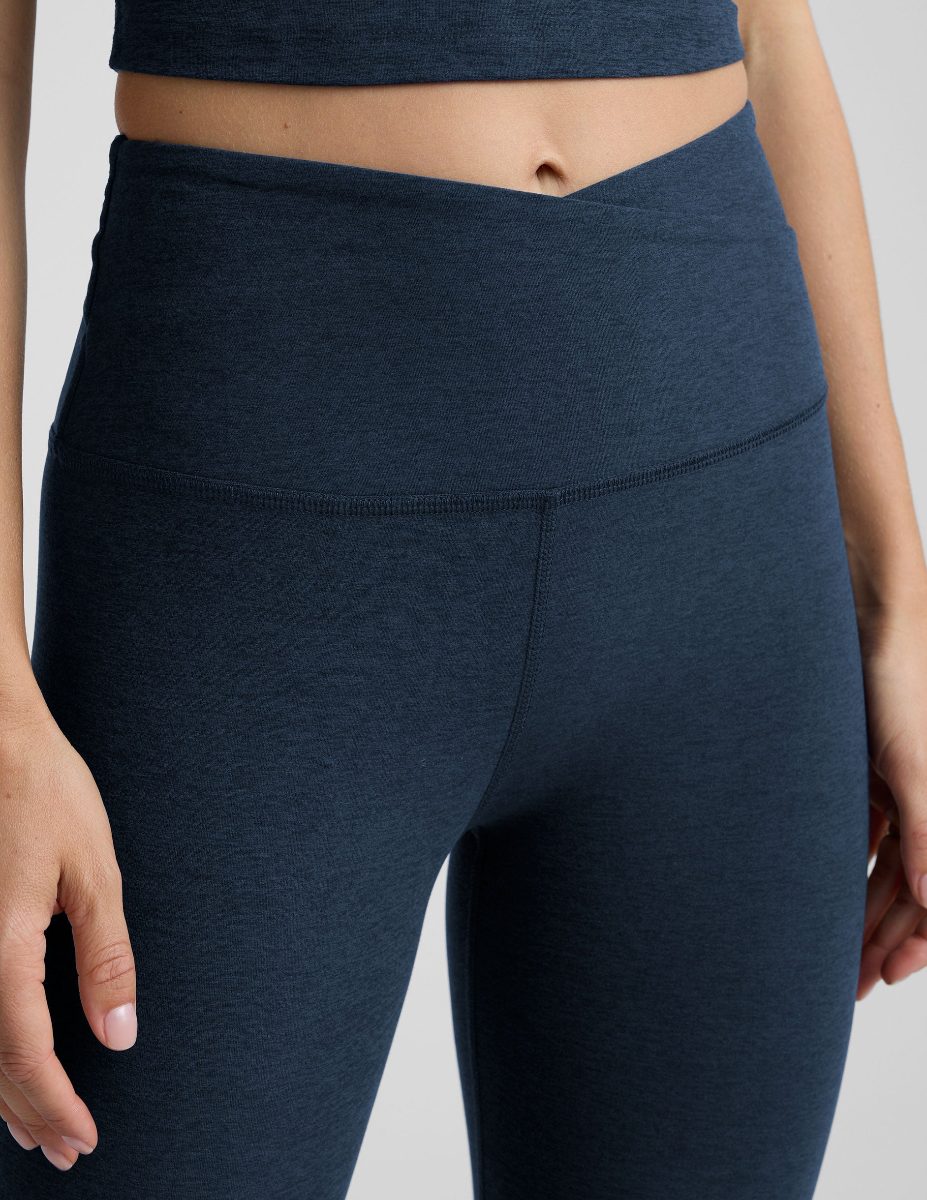 Person wearing navy blue leggings with a front crossover waistband on a plain background.