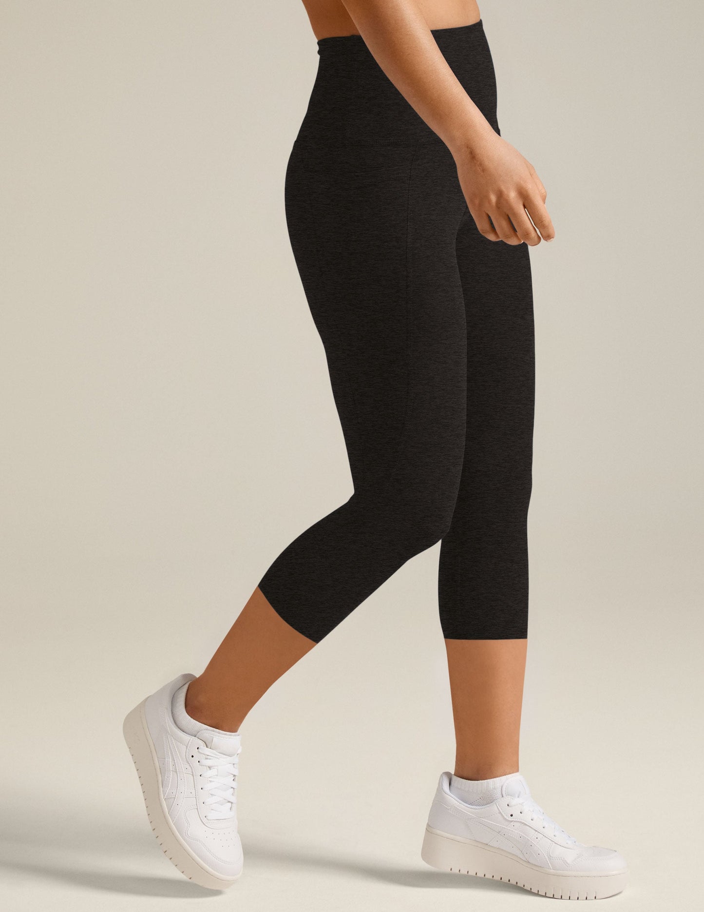 Side view of a person walking in black marled Spacedye Out Of Pocket High Waisted Capri Legging with hip pockets.