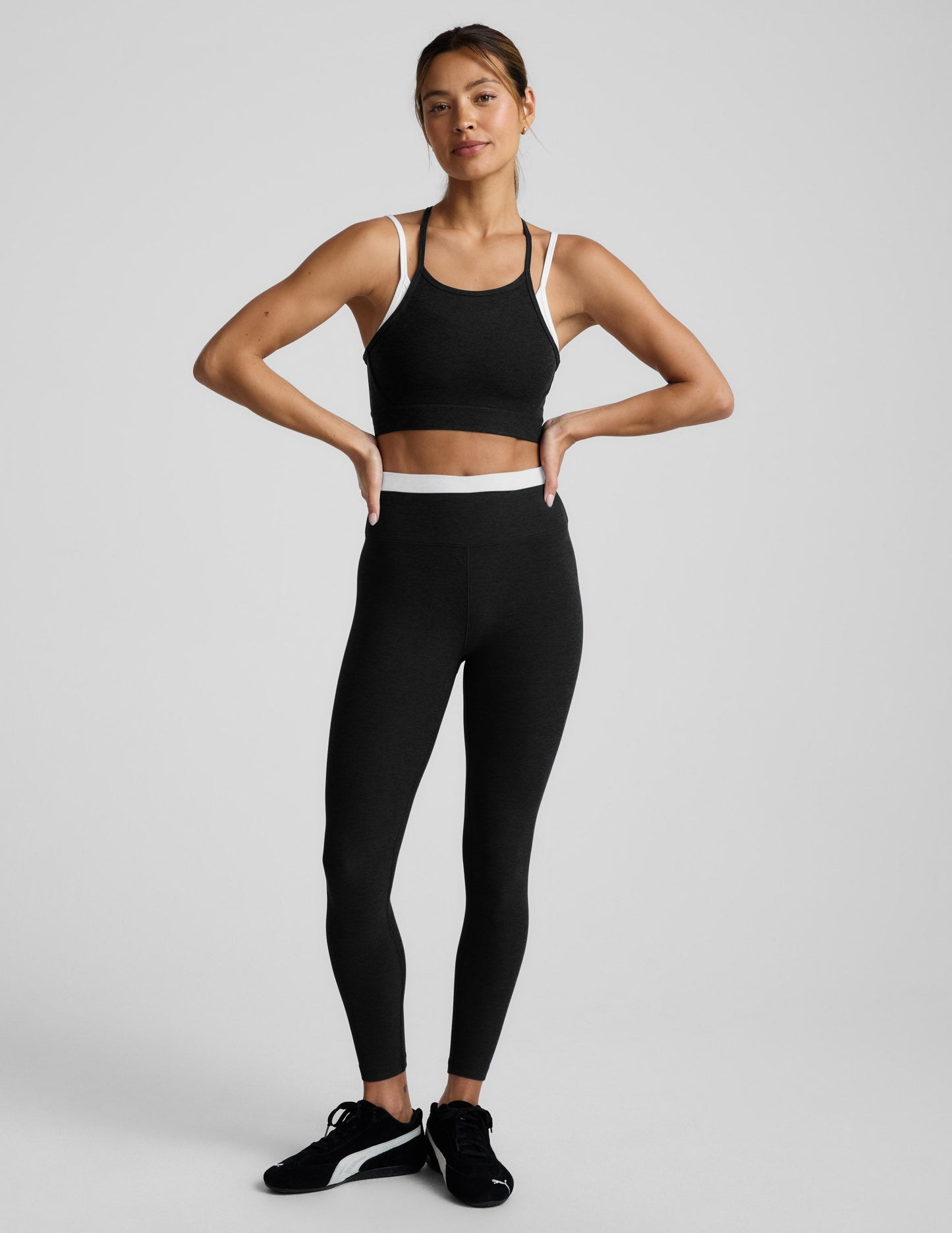 Woman wearing a black sports bra and leggings on a light gray background.