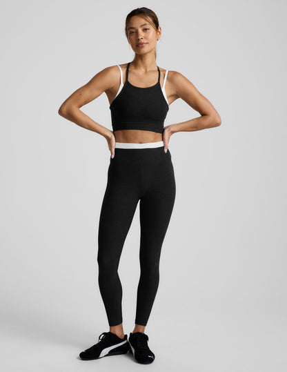 Woman wearing a black sports bra and leggings on a light gray background.