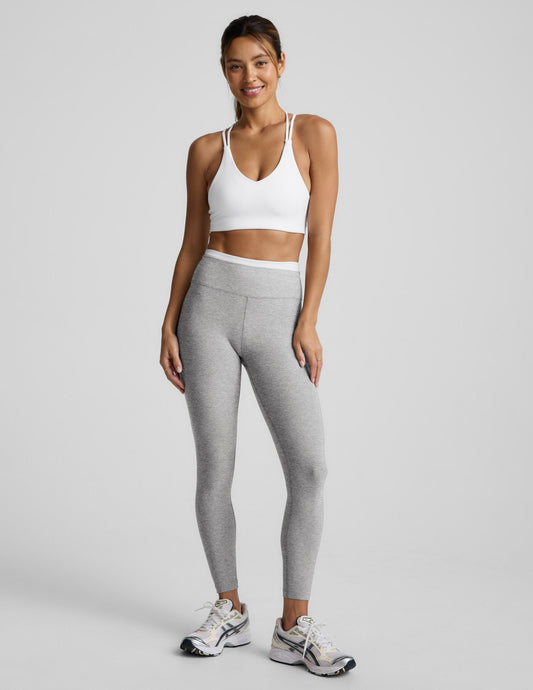 Woman wearing a white sports bra and gray leggings on a light gray background.