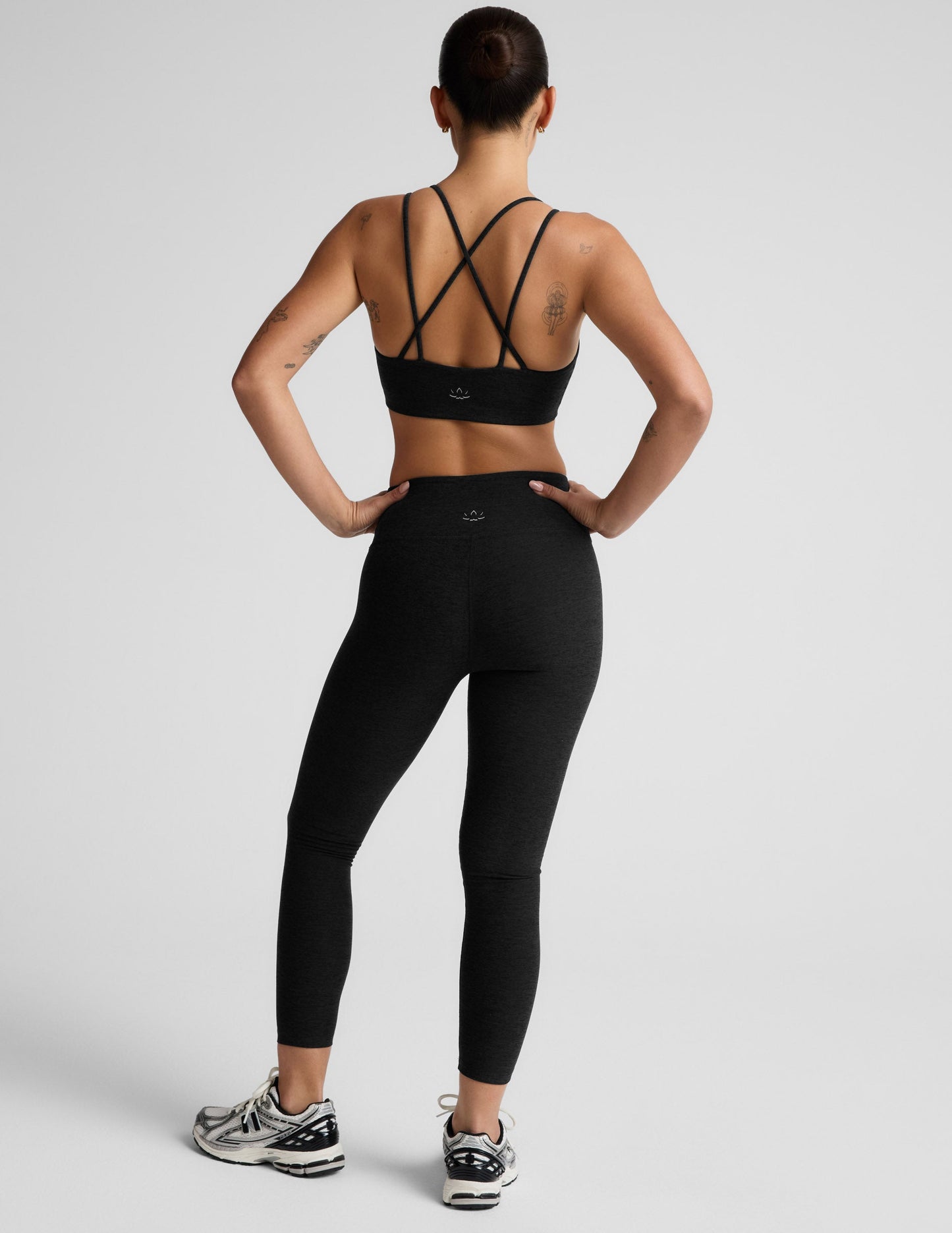 Woman wearing a black sports bra and black mid rise leggings against a light gray background.