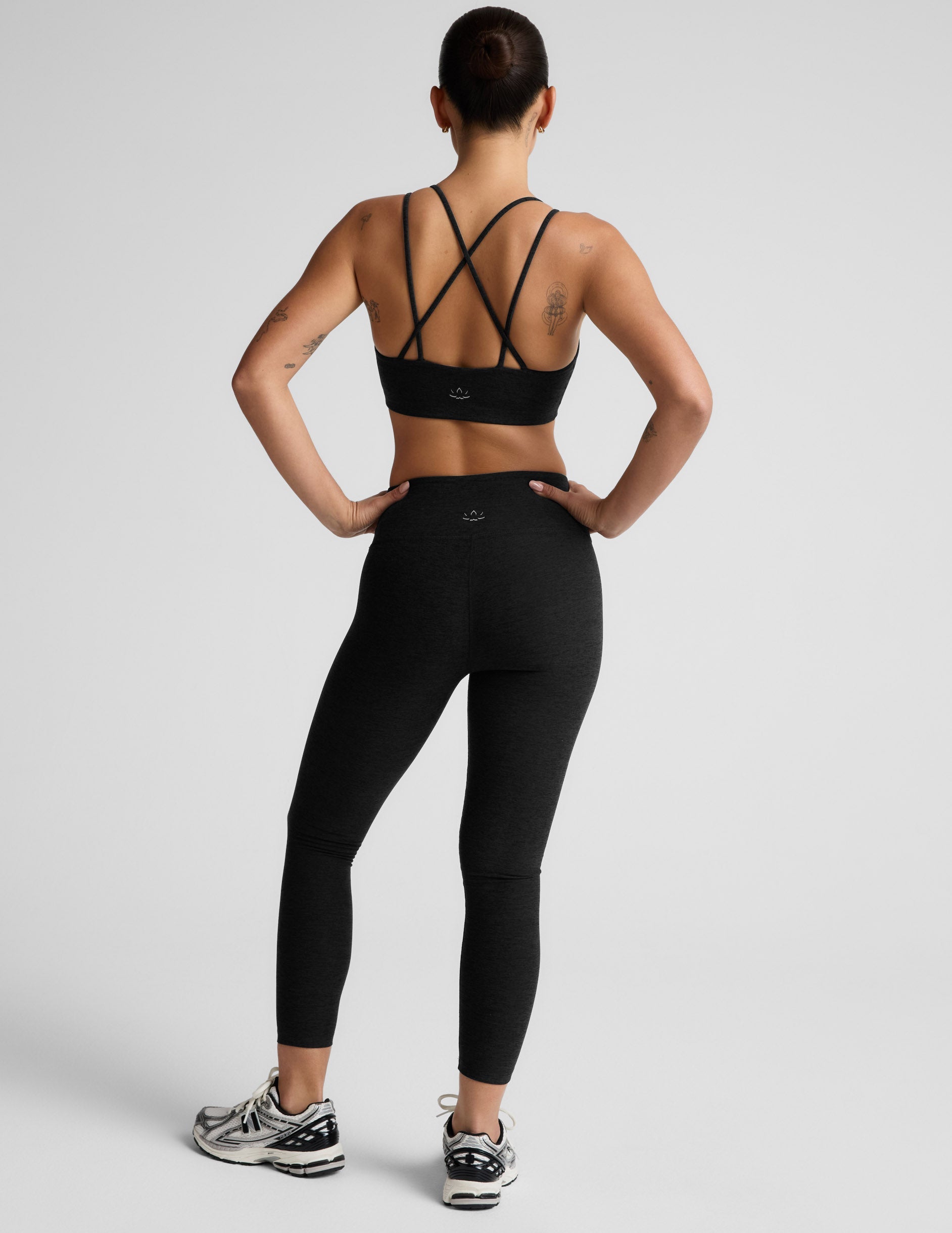Woman wearing a black sports bra and black mid rise leggings against a light gray background.