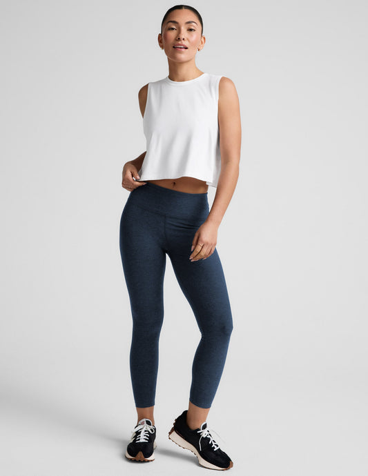 Woman wearing navy midi leggings and a white sleeveless top on a light gray background.