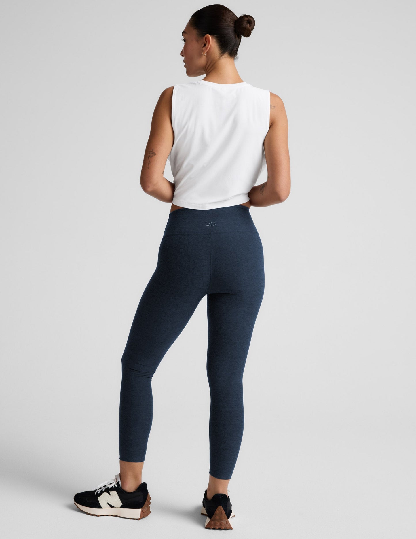 Woman wearing navy midi leggings and a white sleeveless top on a light gray background.