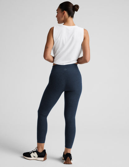 Woman wearing navy midi leggings and a white sleeveless top on a light gray background.