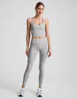 Woman wearing a silver mist cropped racerback tank and mid rise midi length leggings against a plain background.