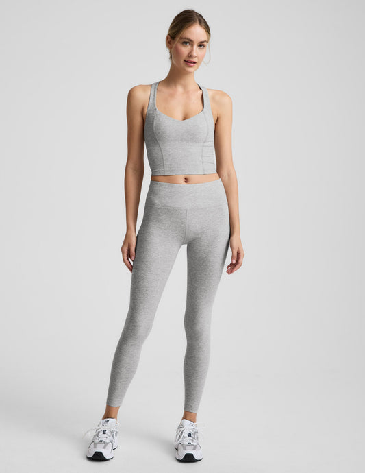 Woman wearing a silver mist cropped racerback tank and mid rise midi length leggings against a plain background.