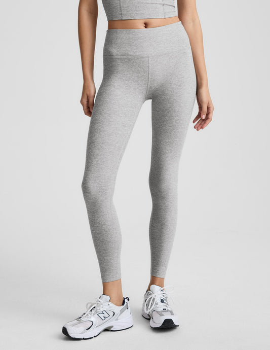 Woman wearing grey mid rise midi length leggings against a plain background.