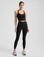 Woman wearing a black cropped tank and black midi length leggings against a plain background.