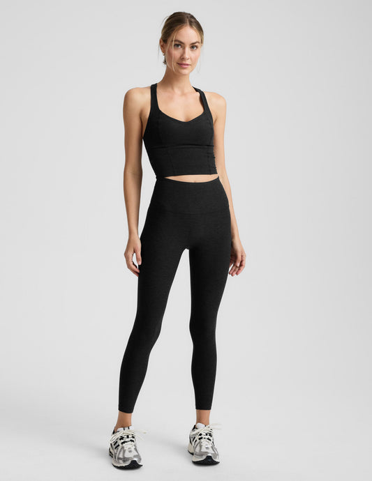 Woman wearing a black cropped tank and black midi length leggings against a plain background.