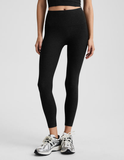 Woman wearing black midi length leggings against a plain background.