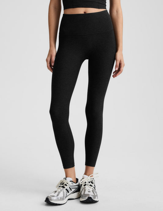Woman wearing black midi length leggings against a plain background.