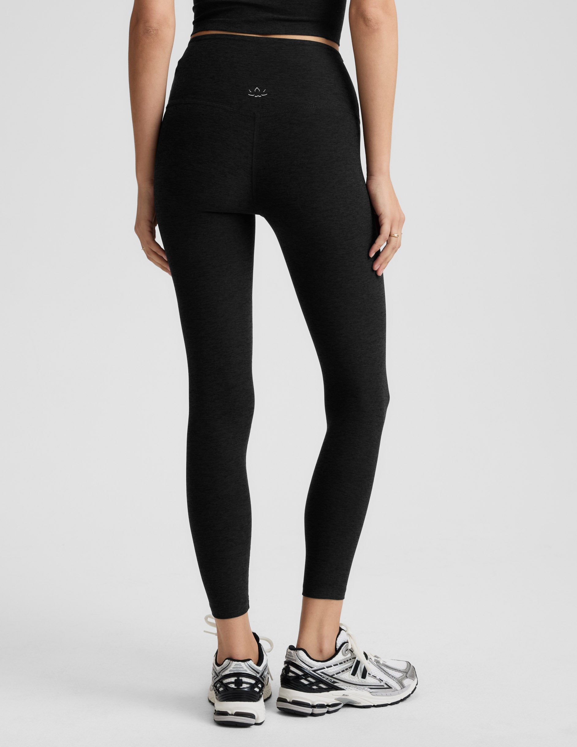 Woman wearing black midi length leggings against a plain background.