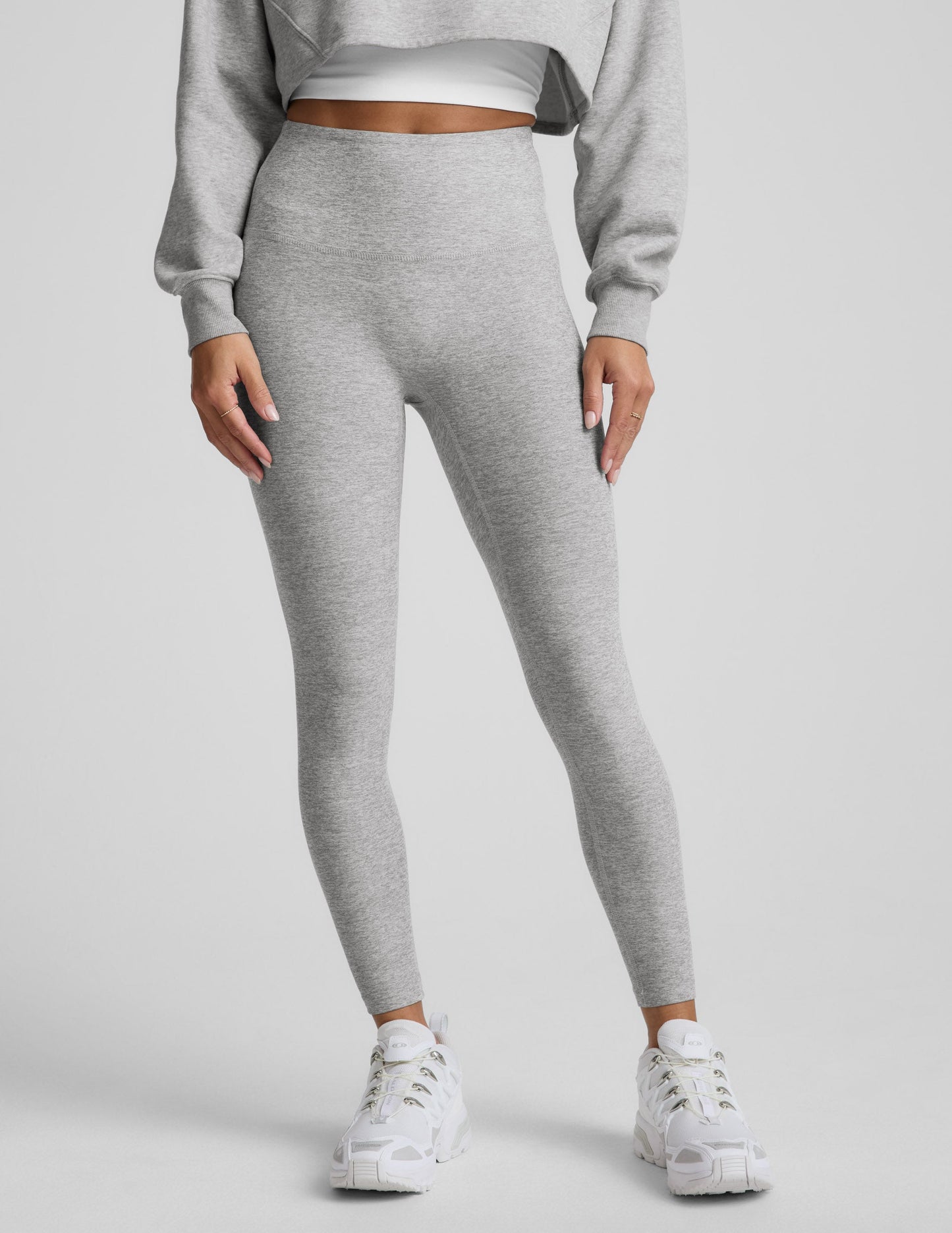 Woman wearing a gray sweatshirt and leggings set on a plain background.