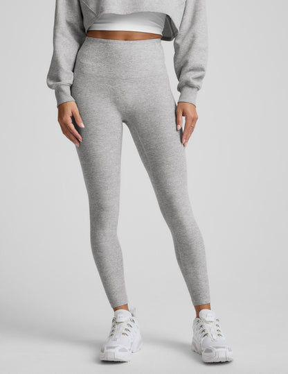 Woman wearing a gray sweatshirt and leggings set on a plain background.