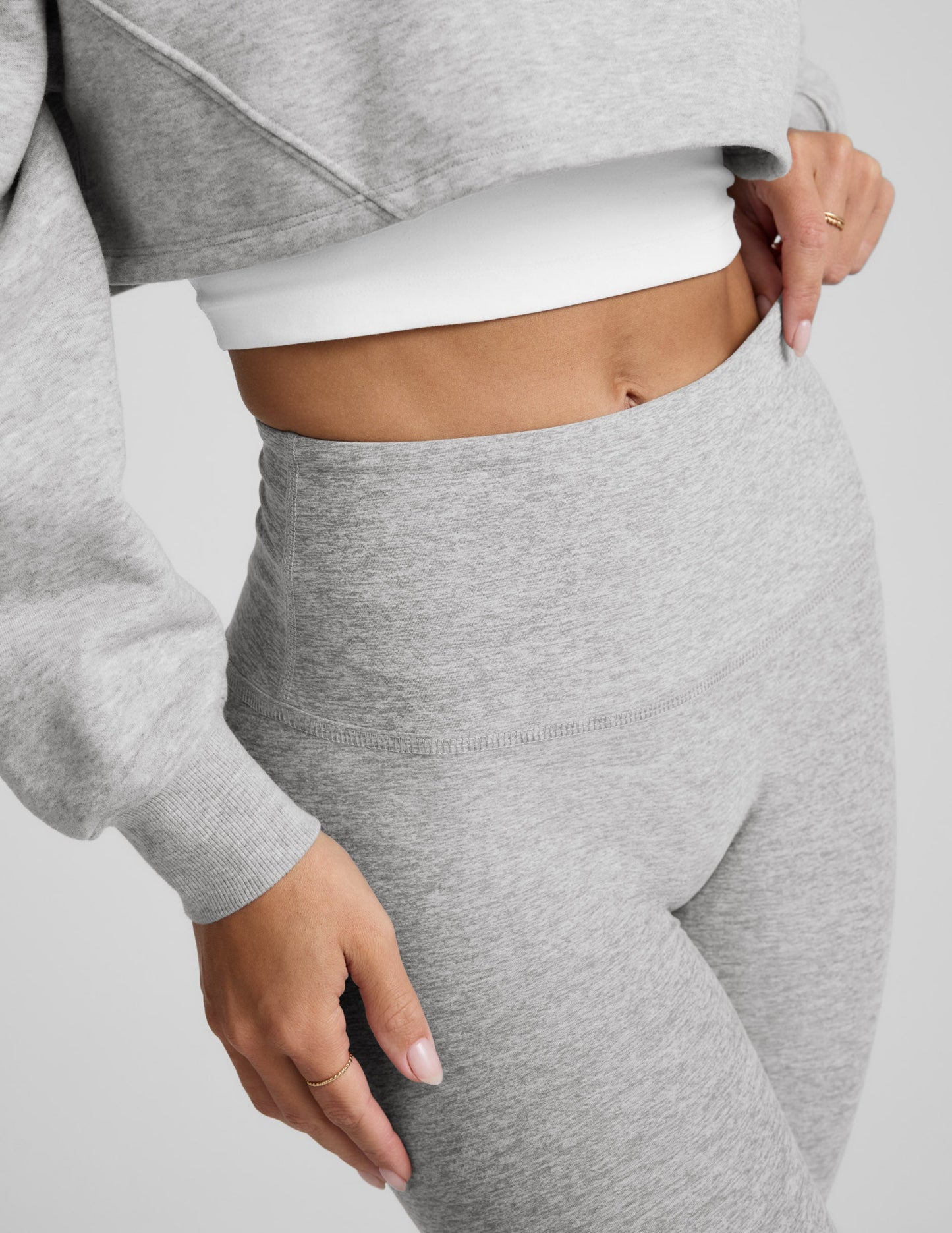 Woman wearing a gray sweatshirt and leggings set on a plain background.