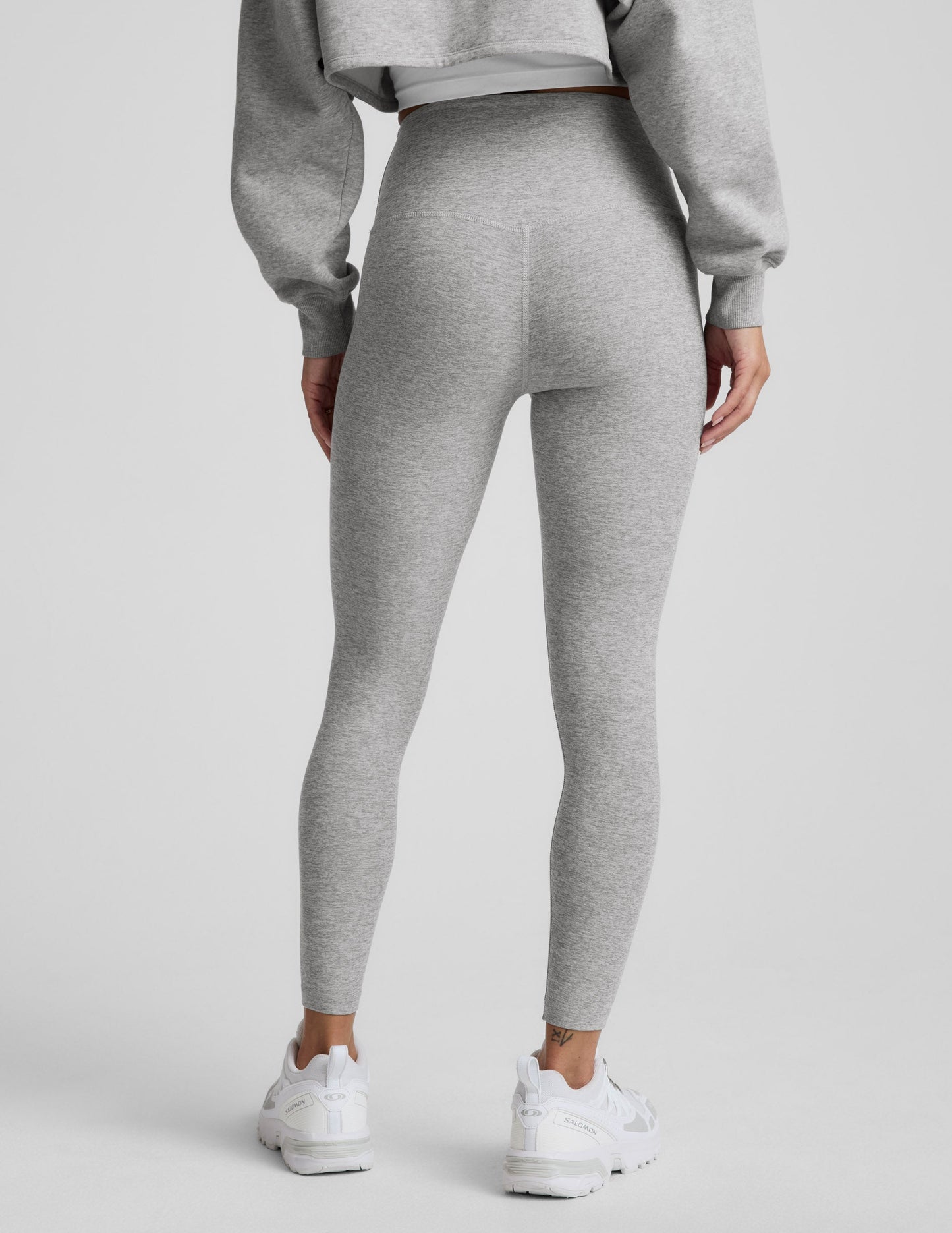 Woman wearing a gray sweatshirt and leggings set on a plain background.