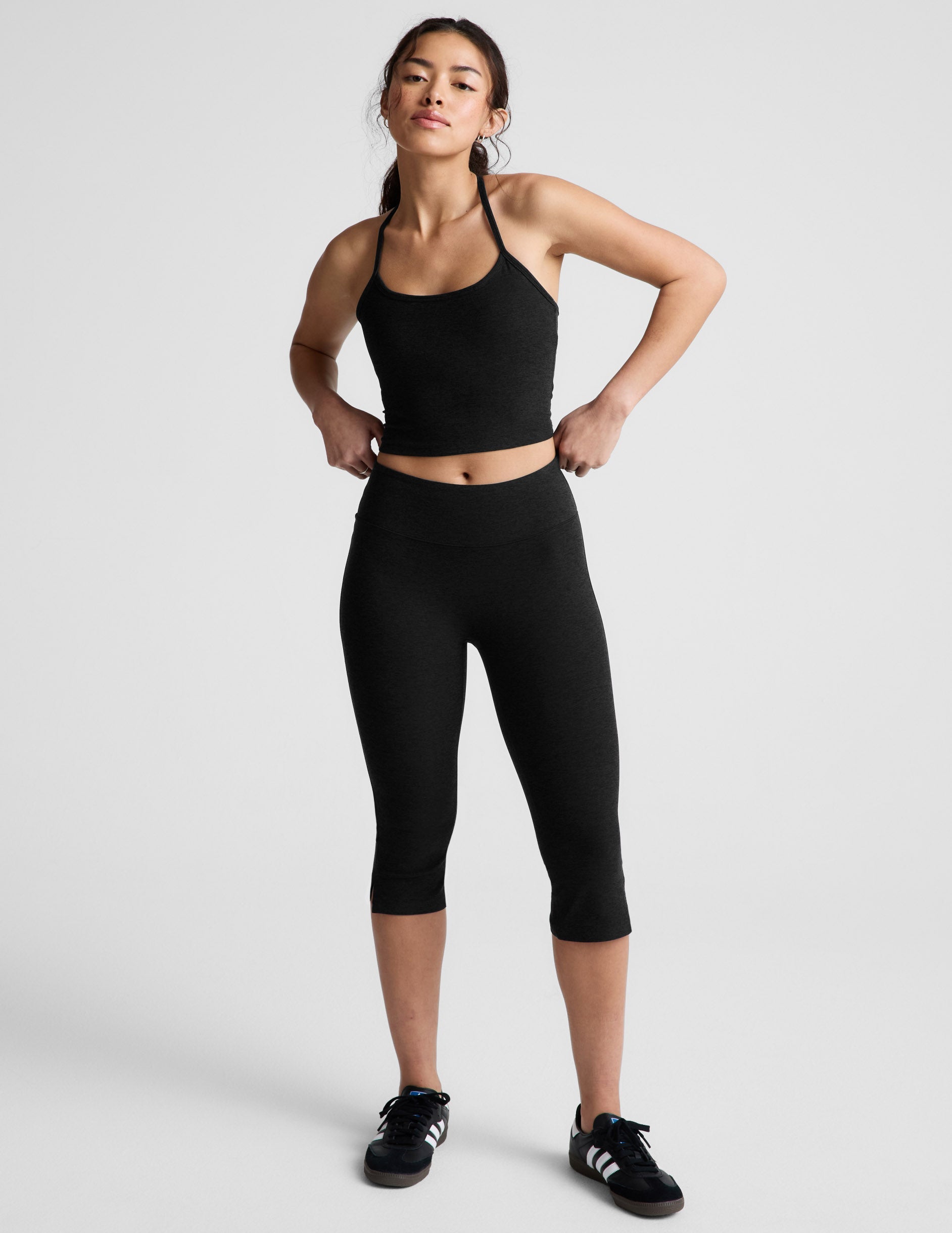 Model wearing Spacedye Mid-Rise Slit Pedal Pusher Legging in black with a matching tank and sneakers on a white background.
