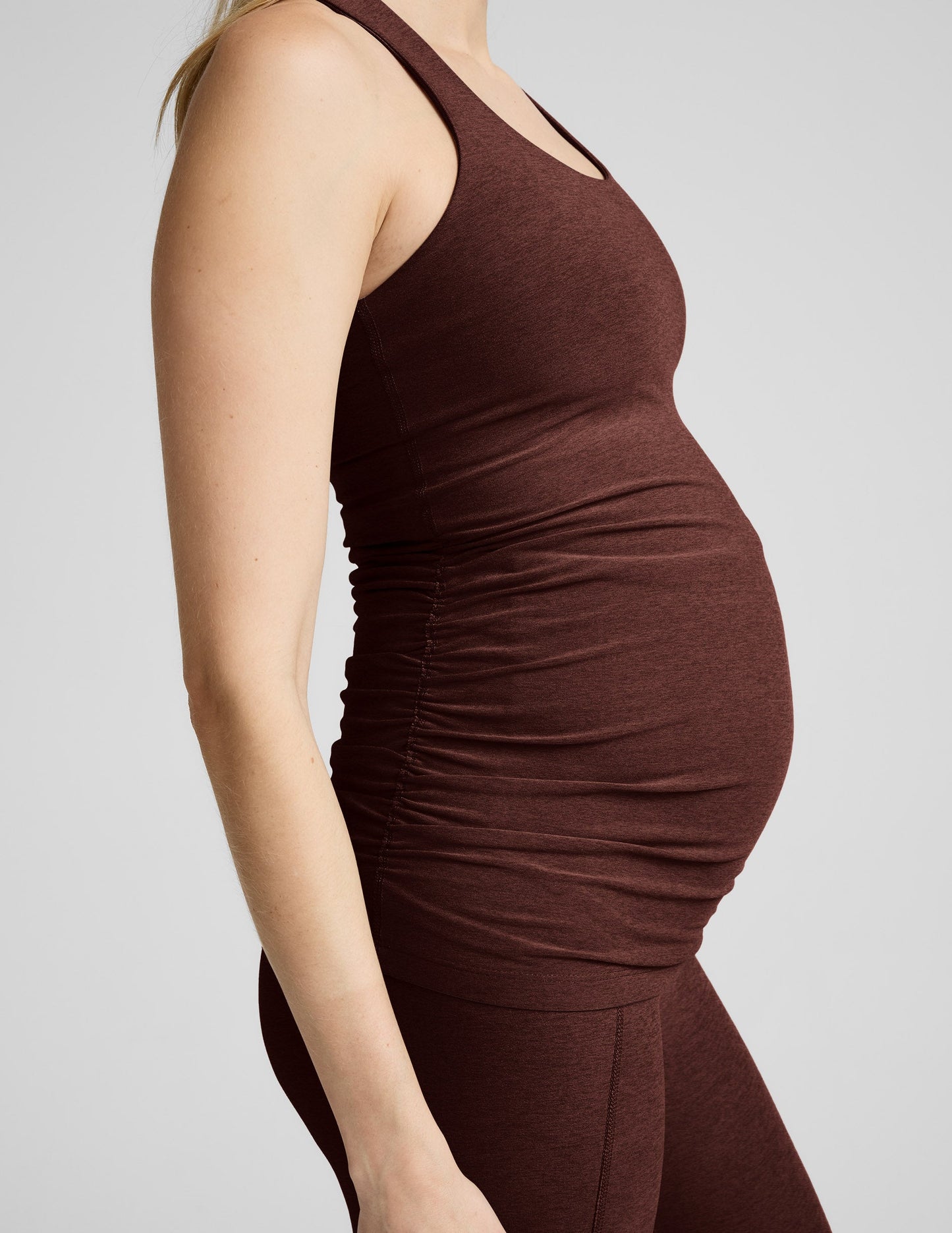 Pregnant woman wearing a brown maternity tank top and brown maternity leggings against a plain background.