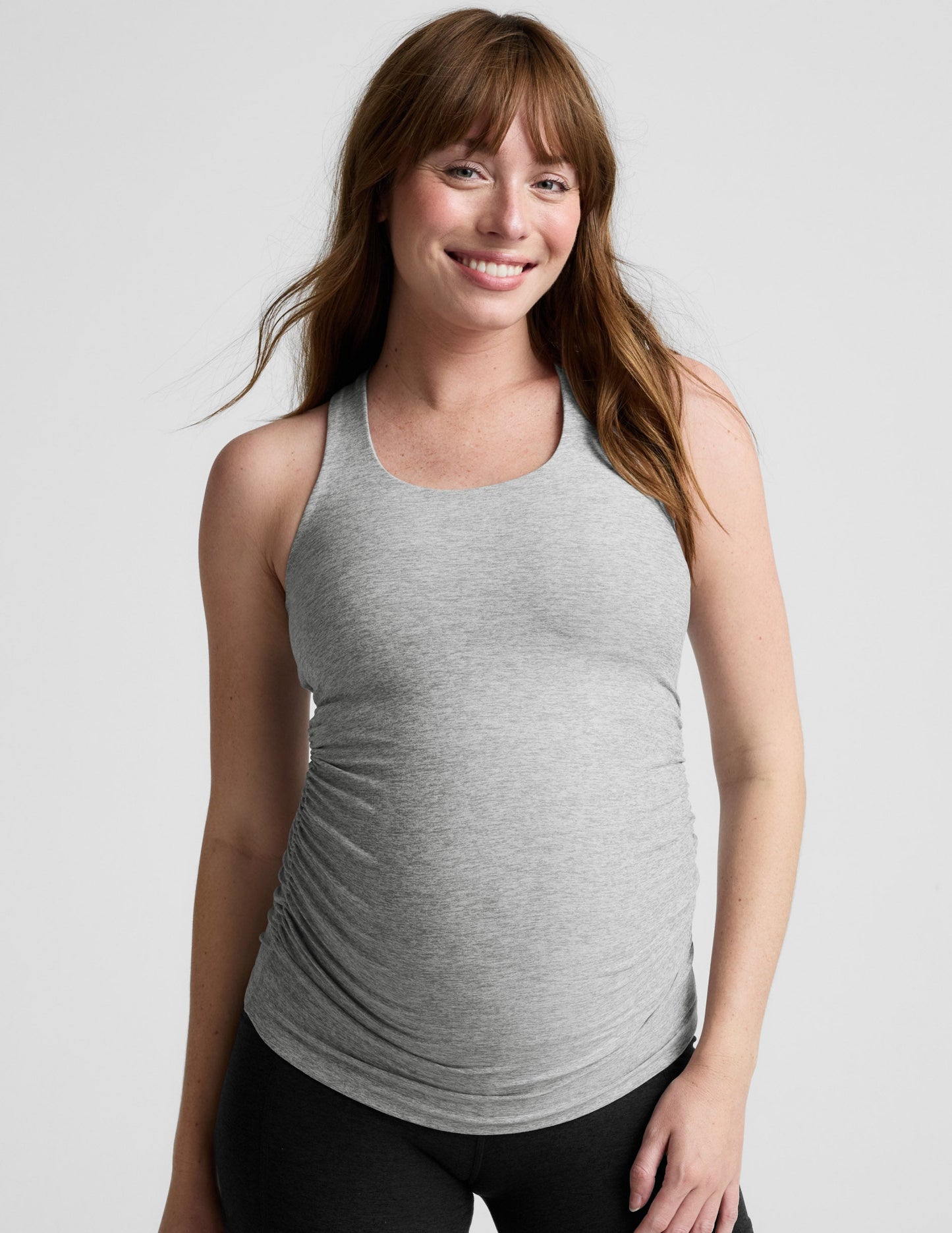 Woman wearing a gray maternity tank top and black shorts on a white background.