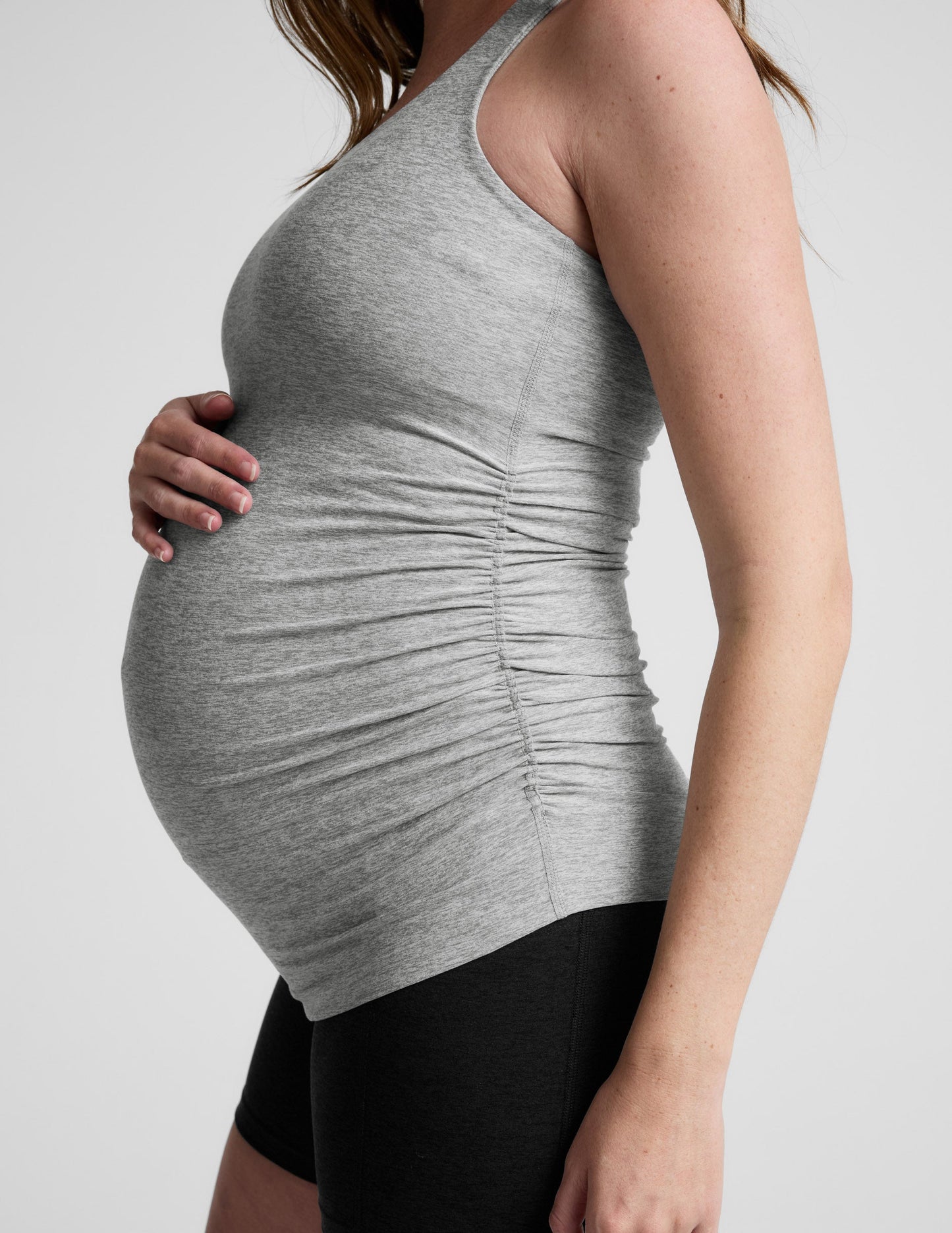 Woman wearing a gray maternity tank top and black shorts on a white background.