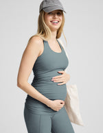 Pregnant woman wearing a gray tank top and cap on a light gray background.