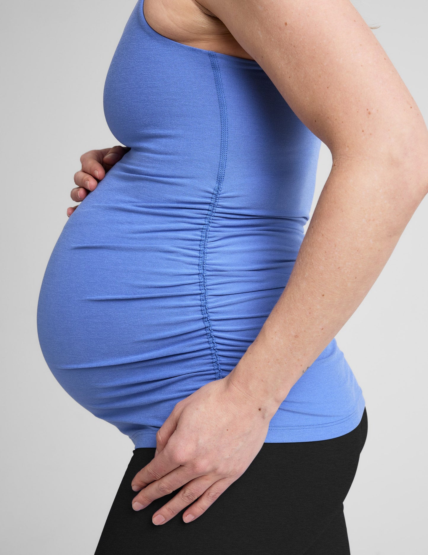 Pregnant woman wearing a blue tank top and black shorts on a white background.