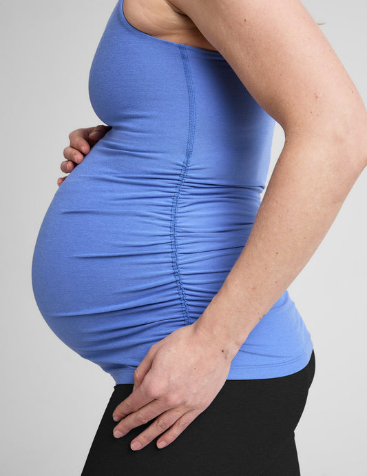 Pregnant woman wearing a blue tank top and black shorts on a white background.
