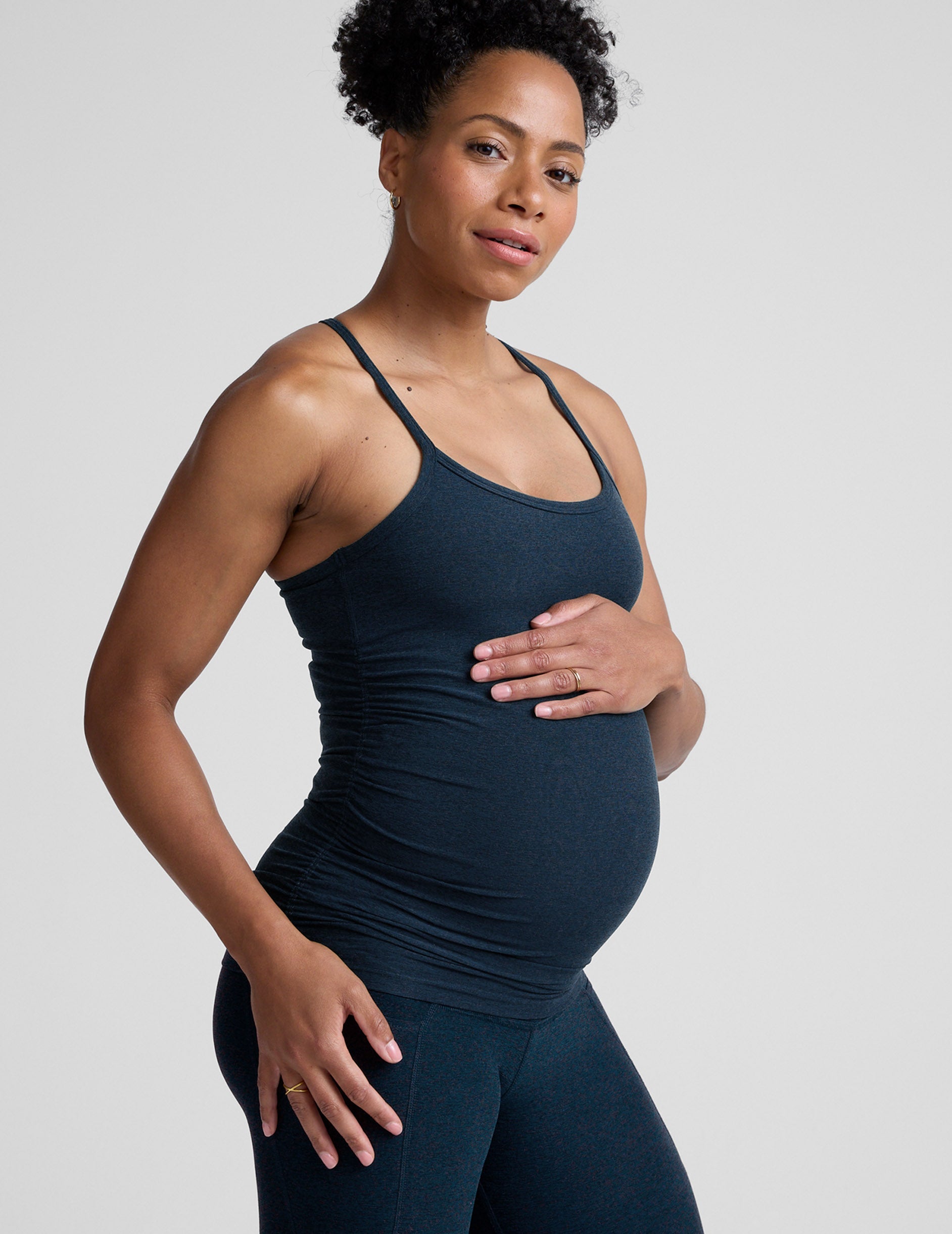 Pregnant woman wearing a dark blue tank top and leggings on a light gray background.