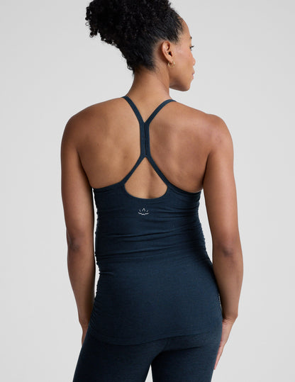 Pregnant woman wearing a dark blue tank top and leggings on a light gray background.